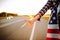 Young female tourist with american flag hitchhiking along a desolate road. Close up woman`s hand showind thumbs up. Face is not