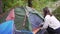 A young female tourist opens a green tent set up in the forest. Traveling in nature. Preparing a place for the night