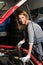 Young female trainee fixing car engine in garage