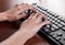 Young female typing on black computer keyboard on wooden desk in office