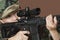 Young female US Marine Corps soldier aiming M4 assault rifle over brown background