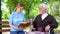 Young female volunteer reading book for disabled pensioner in wheelchair, care