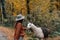 Young female wearing a brown jacket with a fedora hat and feeding a llama in a forest in autumn