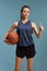 Young female wearing shorts and jersey holding a basketball and showing thumbs up