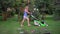 Young female woman pushing grass trimming lawnmower through garden