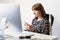 Young female worker at desk in modern minimalistic office. Portrait of business woman using mobile phone in front of desktop comp