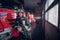 Young fireman wearing protective uniform standing next to a fire engine in a garage of a fire department