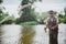 Young fisherman fishing on lake or river. Serious concentrated guy in fisherman`s clothes stand in river or lake water