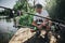 Young fisherman fishing on lake or river. Serious concentrated professional adult guy sitting in squat position at