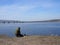 Young fisherman in a green hoodie sits on the river Bank near the bridge in spring