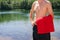 Young and fit, athletic male man standing on the lake shore without a shirt while holding red towel. Swimming, summer activities