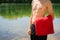 Young and fit, athletic male man standing on the lake shore without a shirt while holding red towel. Swimming, summer activities