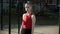 Young fit blond busty woman with ponytail in red top stands at sports ground