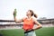 Young fit blond woman, wearing orange top and green leggings, drinking savoring water from light green bottle, smiling. Refresh