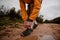 Young fit male athlete bending over tying shoe laces of running shoes while running on wet mountain path in cloudy