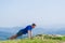 A young fit male athlete is doing push-ups outdoors on a cliff while looking at the breathtaking mountain line