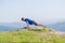 A young fit male athlete is doing push-ups outdoors on a cliff while looking at the breathtaking mountain line