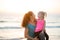 Young fit mother smiling with daughter on her knee on beach