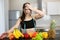 Young fit woman with centimeter round neck wearing black sports top standing in the kitchen full of fruits looks desperate