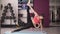 Young fit woman demonstrate side plank. Stretching on a blue mat, holding leg. Studio with dumbbells, front view