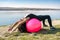 Young fit woman in sportswear during fitness time and exercising with ball at the lake. Healthy lifestyle