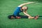 Young fitness girl with closed eyes in a blue shirt and leggings doing stretching in the sunset . Football field.