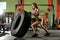 Young fitness woman execute exercise with large tire casing, in