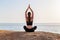 Young fitness woman meditationg in lotus pose at the beach in the morning