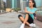 Young fitness woman resting after exercising, sitting at the bench in city center.