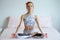 Young fitness woman in sportwear practicing yoga on bed in bedroom at home in Morning . sport girl doing meditating in lotus pose