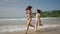 Young fitted women in swimwear holding hands, running along sea water edge. Smiling pretty girls fooling, making water