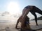 Young flexible caucasian girl practice wheel yoga pose at seaside in sunshine