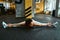 Young flexible fitness woman in sportswear sitting on the floor at gym and practicing transverse twine, stretching