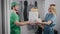 A young food delivery man in a green uniform. A man brought pizza and a bag of food to a beautiful woman.