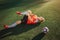 Young football player lying on lawn and hold leg. He pulls it to himself. Guy feels pain in knee. Ball lying besides him.