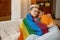 Young freedom lesbian woman cuddling in lgbt rainbow flag while sitting on sofa