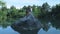 A young freelance guy sits on a stone in the middle of a lake with a laptop. Freelance concept. Work on travel. Wireless