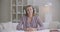 Young friendly woman is listening interlocutor by video chat by headphones and nodding looking at camera