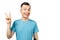 Young funny caucasian guy in blue t-shirt shows a peace sign and smiles, on isolated white background