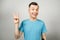 Young funny caucasian guy in blue t-shirt shows a peace sign and smiles, on light gray background