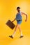 Young funny man wearing retro striped swimsuit and vintage bowler hat holding old suitcase isolated on bright yellow