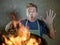 Young funny and messy home cook man with apron in shock holding pan in fire burning the food in kitchen disaster and domestic cook