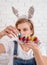 Young funny woman in bunny ears putting a colored quail egg into the plastic holder