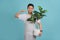 Young gardener Asian man holding a plant isolated on light blue background. He pointing by hand to a shirt copy space, proud and