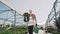 The young gardener goes greenhouse, holds in the hands of a green pot and funnel. Stabilized camera movement, overall