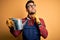 Young gardener man wearing working apron and gloves holding watering can serious face thinking about question, very confused idea