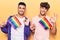 Young gay couple holding rainbow lgbtq flags doing ok sign with fingers, smiling friendly gesturing excellent symbol