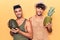 Young gay couple wearing summer clothes holding melon and pineapple looking positive and happy standing and smiling with a