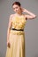 Young ginger lady in yellow evening dress with pleating skirt, high halter neckline and black belt on thin waist.