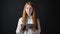 Young ginger teenage girl in white shirt typing on tablet and looking at camera, standing isolated on black background